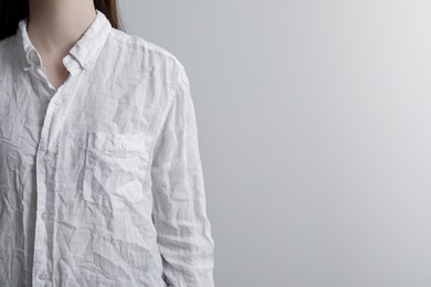 Woman wearing wrinkled white blouse on light grey background, closeup. Space for text