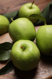 Photo of Ripe green apples with leaves and water drops on wooden board, closeup