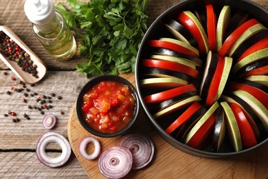 Photo of Cooking delicious ratatouille. Different fresh vegetables and round baking pan on wooden table, flat lay