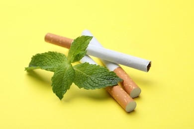Photo of Menthol cigarettes and mint on yellow background