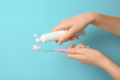 Woman squeezing toothpaste on brush against color background