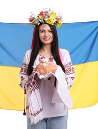 Young woman in national clothes with traditional korovai and flag of Ukraine on white background