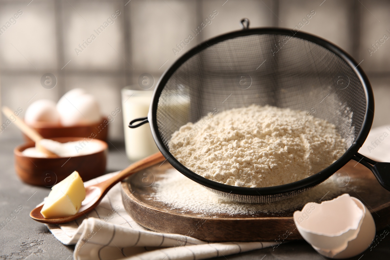 Photo of Making dough. Flour in sieve, spoon and butter on grey table, closeup