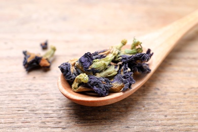 Photo of Spoon with dry organic blue Anchan on wooden table, closeup. Herbal tea