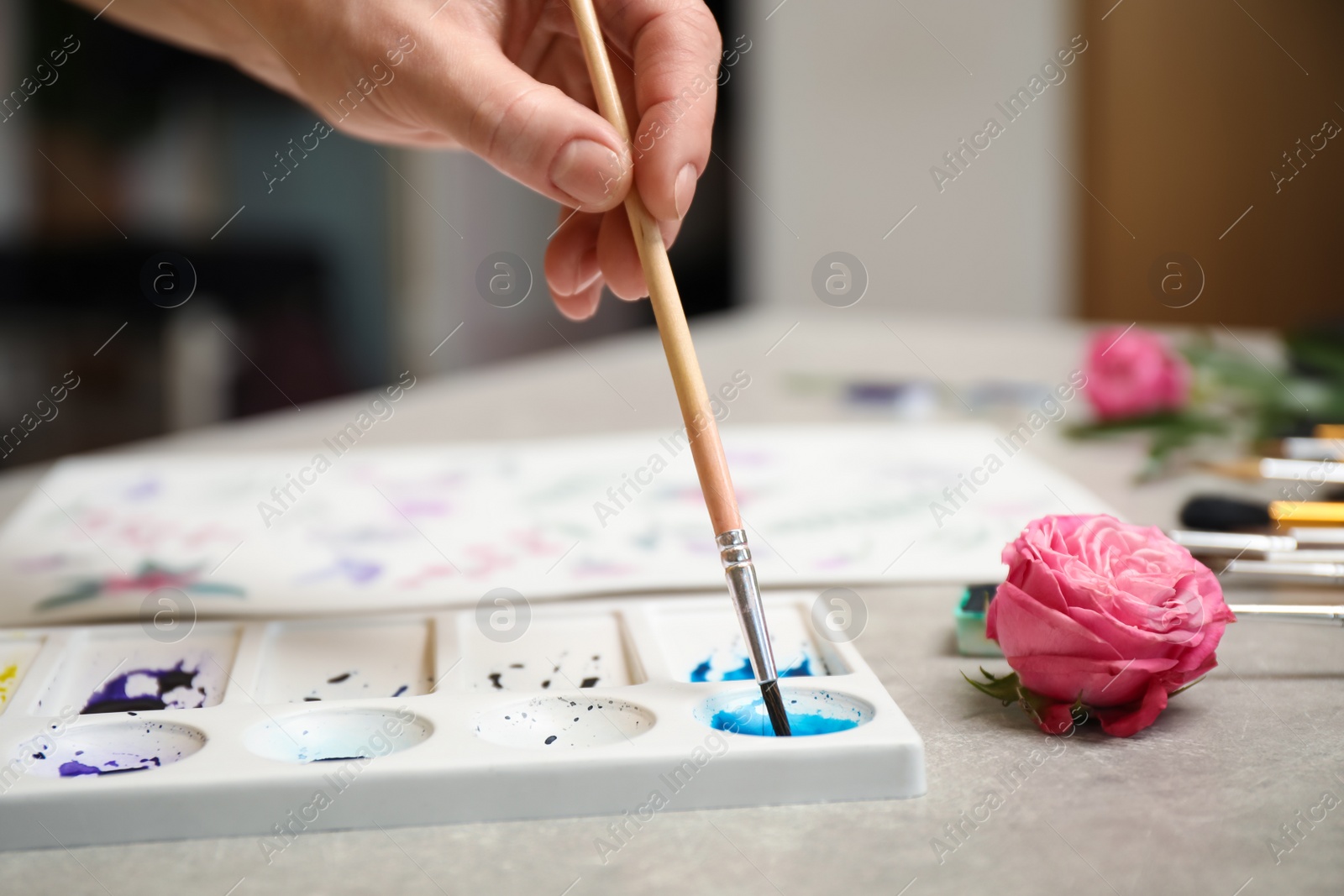 Photo of Woman painting with watercolor at grey stone table, closeup