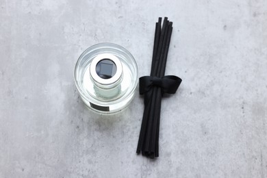 Photo of Reed sticks near glass bottle with aromatic liquid on gray marble table, flat lay
