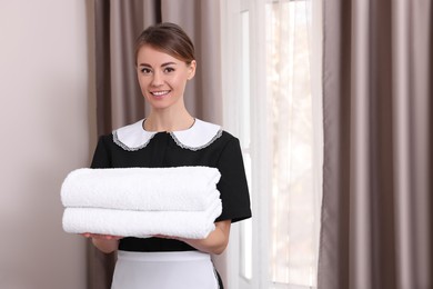 Photo of Beautiful chambermaid with stack of fresh towels in hotel room