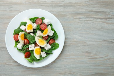Delicious salad with boiled eggs, feta cheese and tomatoes on wooden table, top view. Space for text