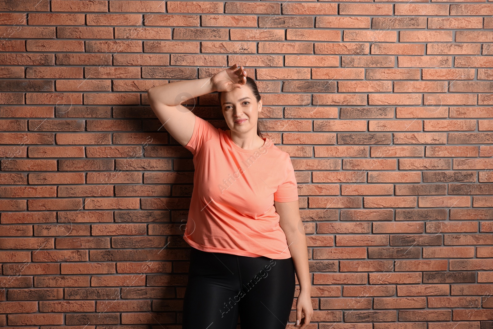 Photo of Happy overweight woman near red brick wall