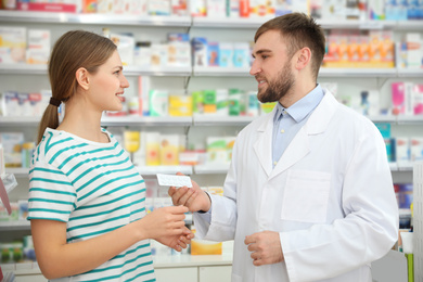 Image of Professional pharmacist giving pills to customer in modern drugstore