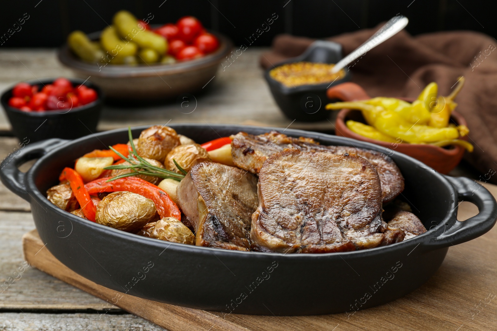 Photo of Tasty beef tongue pieces with potatoes, pepper and rosemary on wooden board, closeup