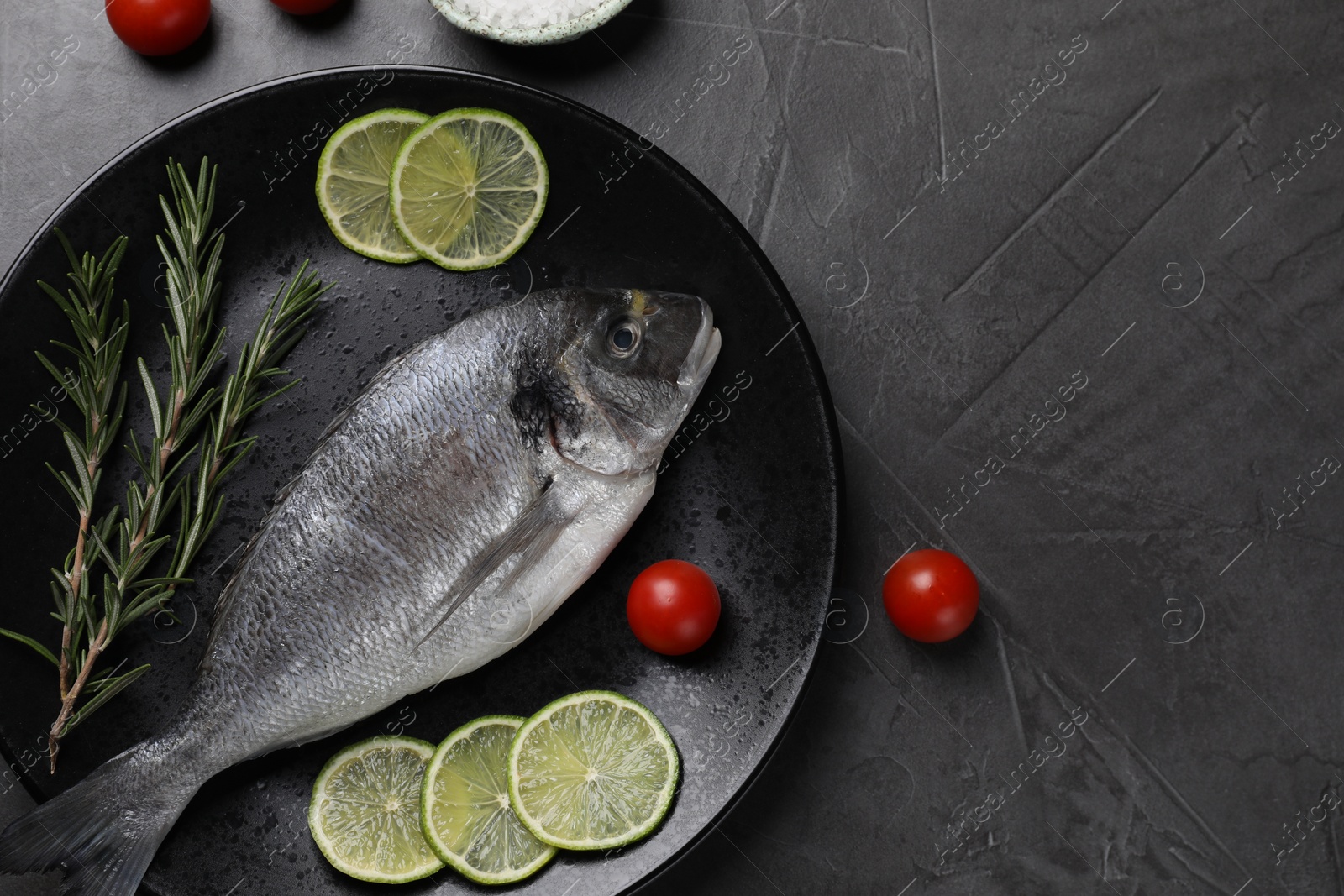 Photo of Fresh dorado fish, lime, tomatoes and rosemary on grey table, top view. Space for text