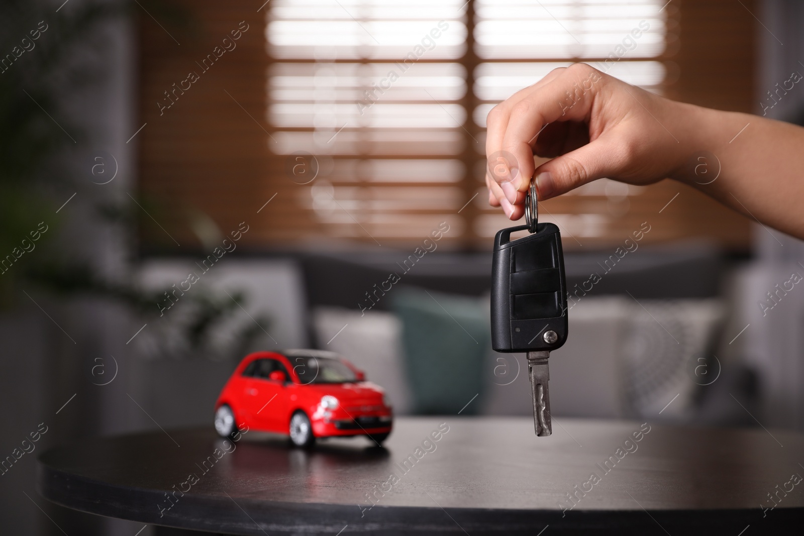 Photo of Man holding key near table with miniature automobile model indoors, closeup. Car buying