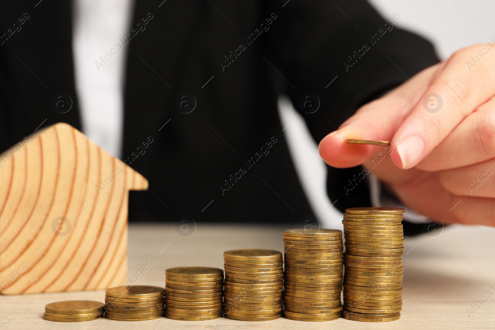 Photo of Mortgage concept. Woman stacking coins near house model at wooden table, closeup