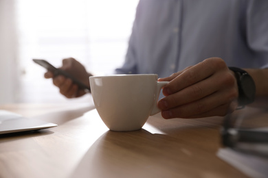 Man with cup of coffee at table indoors, closeup