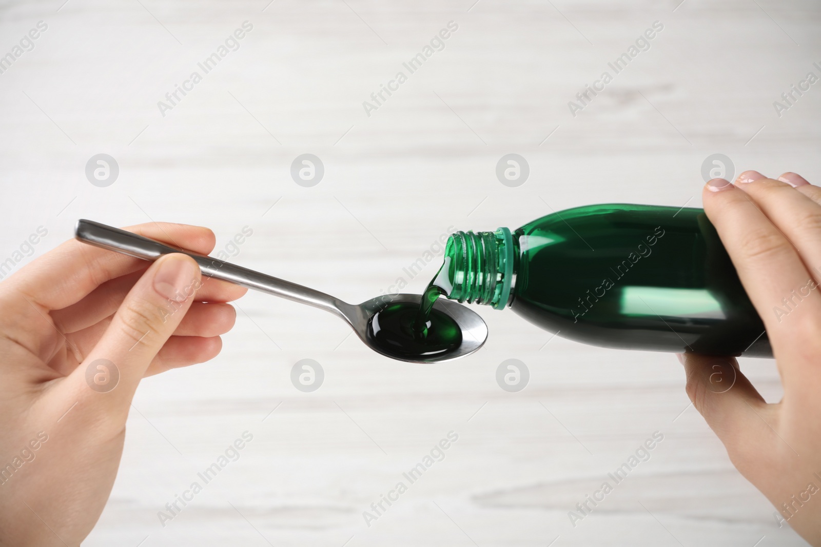 Photo of Woman pouring cough syrup into spoon on light background, closeup