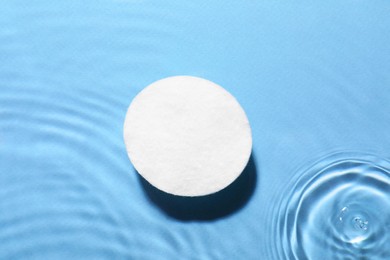 Image of Cotton pad in micellar water on light blue background, top view
