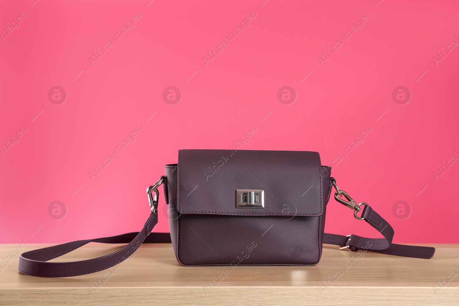 Photo of Stylish woman's bag on wooden table against pink background