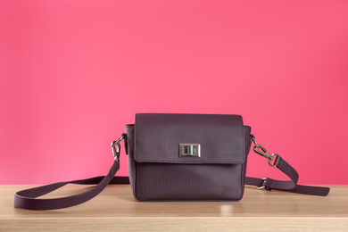 Stylish woman's bag on wooden table against pink background