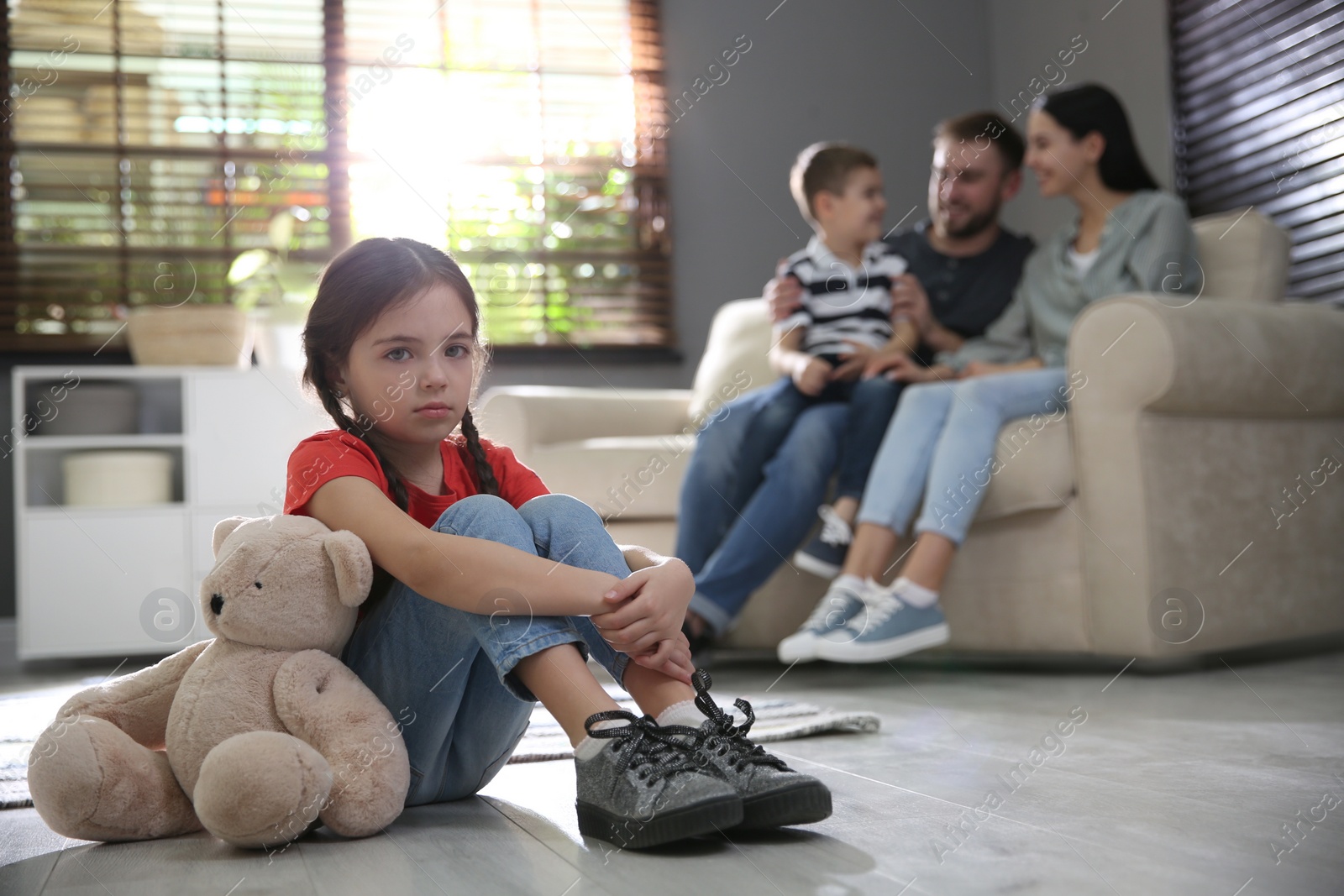 Photo of Unhappy little girl feeling jealous while parents spending time with her brother at home