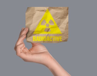Image of Woman holding crumpled paper with hazard symbol and word Radioactive on light grey background, closeup