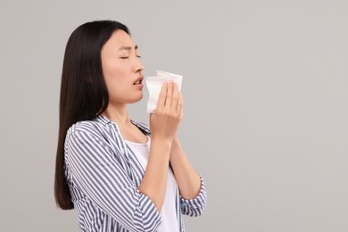 Photo of Suffering from allergy. Young woman with tissue sneezing on grey background, space for text