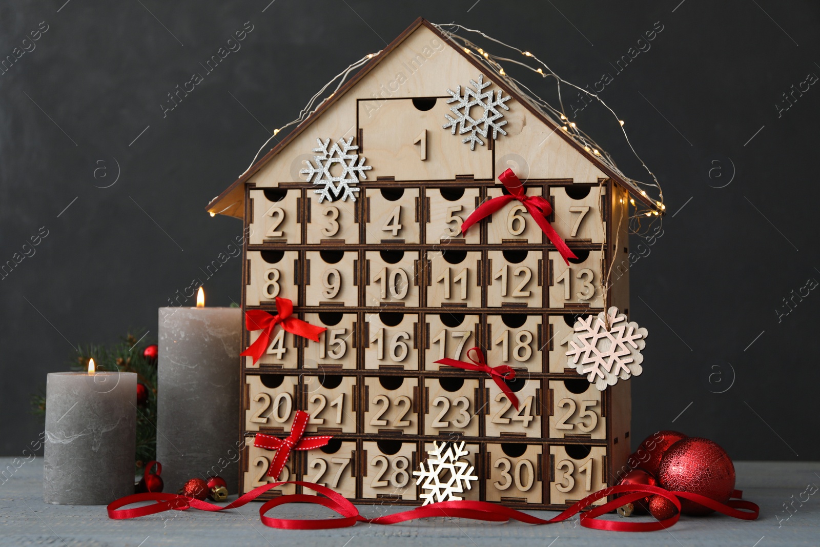 Photo of House shaped Christmas advent calendar and burning candles on grey wooden table