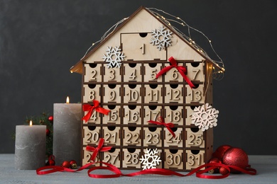 House shaped Christmas advent calendar and burning candles on grey wooden table