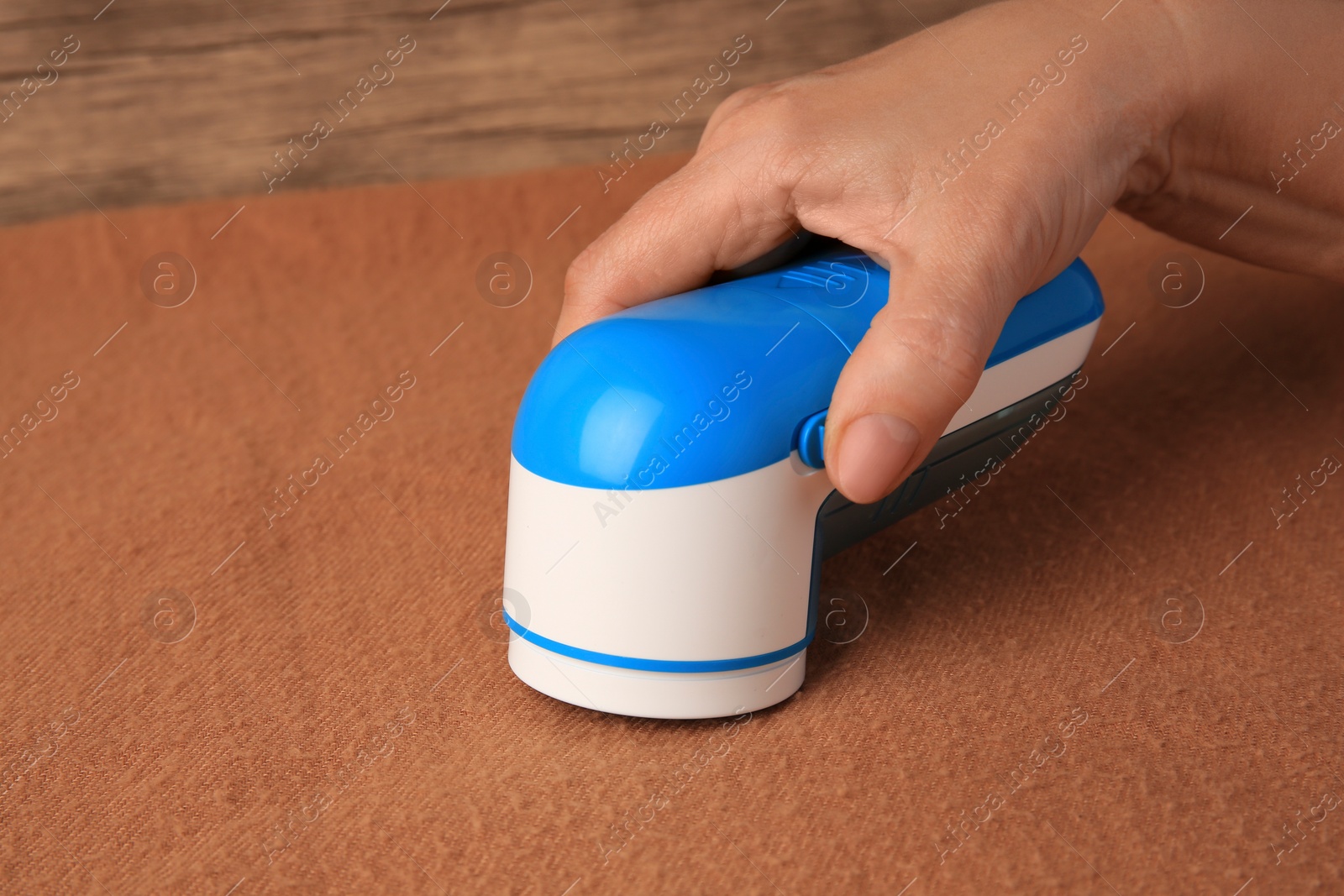 Photo of Woman cleaning brown cloth with fabric shaver at wooden table, closeup