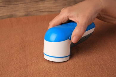 Photo of Woman cleaning brown cloth with fabric shaver at wooden table, closeup