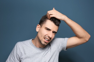 Young man with hair loss problem on color background