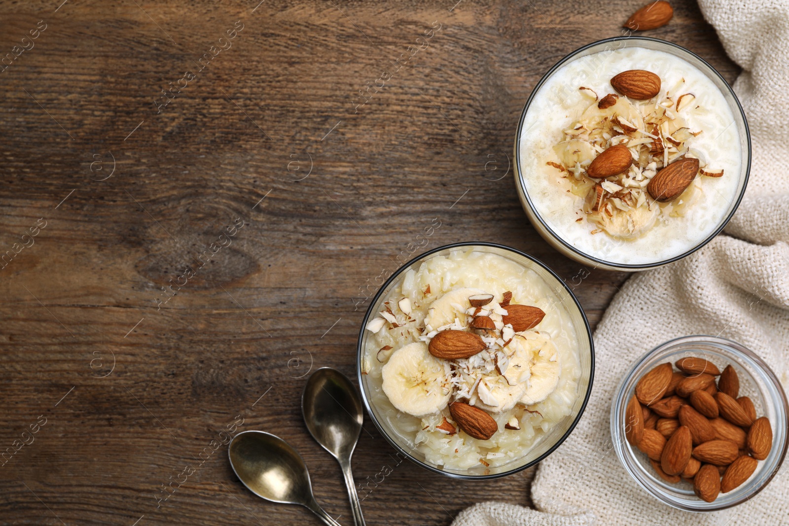 Photo of Delicious rice pudding with banana and almonds on wooden table, flat lay. Space for text