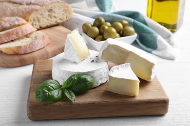Photo of Tasty brie cheese with basil on white wooden table
