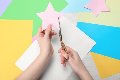 Woman cutting paper star with scissors at white wooden table, top view