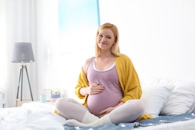 Beautiful pregnant woman sitting on bed in light room