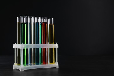 Photo of Many test tubes with liquids in stand on black background, space for text