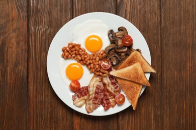 Plate with fried eggs, mushrooms, beans, tomatoes, bacon and toasts on wooden table, top view. Traditional English breakfast