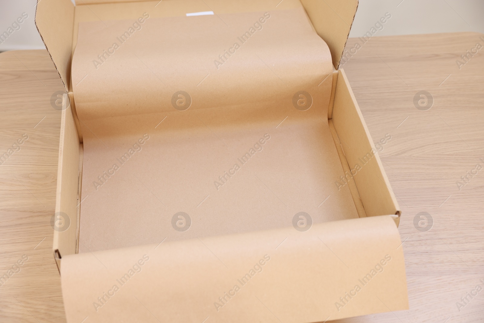 Photo of Empty cardboard box with kraft paper on wooden table, closeup. Delivery service