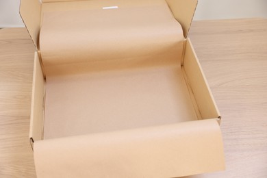 Photo of Empty cardboard box with kraft paper on wooden table, closeup. Delivery service