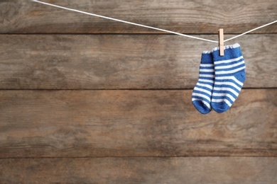 Pair of socks on laundry line against wooden background, space for text. Baby accessories