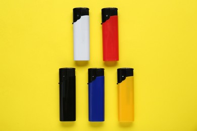 Stylish small pocket lighters on yellow background, flat lay