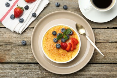 Photo of Delicious creme brulee with berries and mint in bowl on wooden table, flat lay