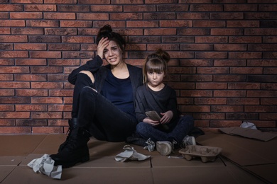 Poor mother and daughter sitting on floor near brick wall