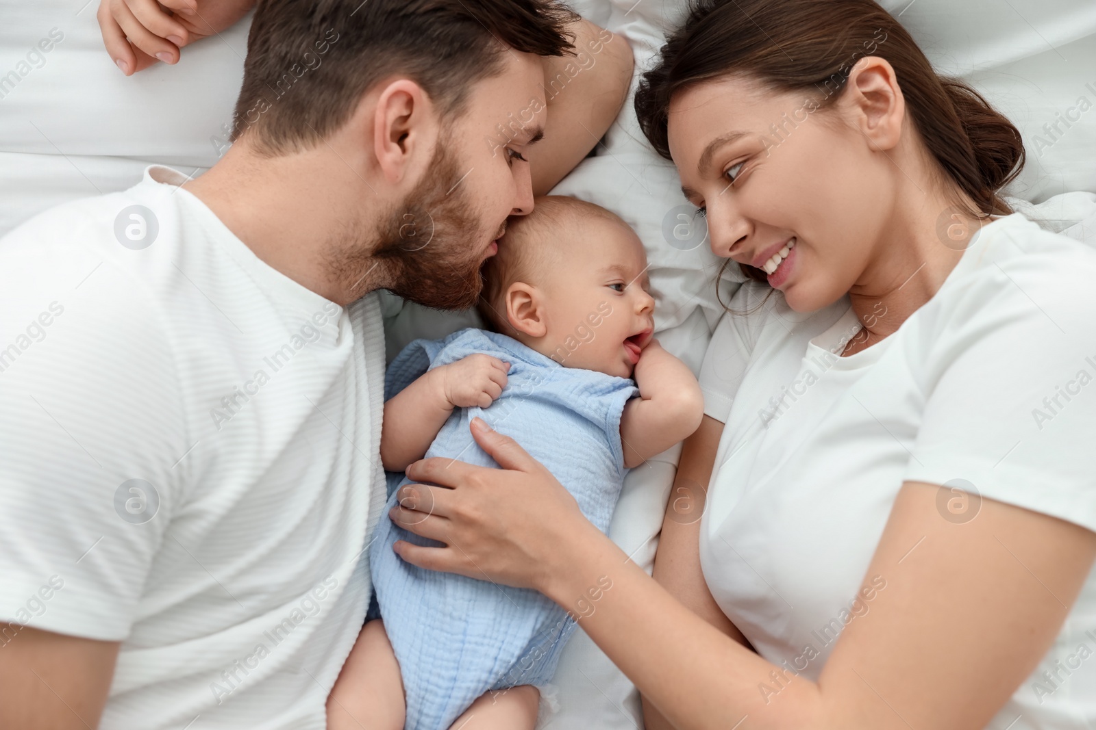 Photo of Happy family. Parents with their cute baby on bed, top view