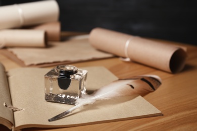 Feather pen, inkwell and open notebook on wooden table