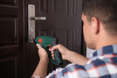 Photo of Handyman with screw gun repairing door lock, closeup