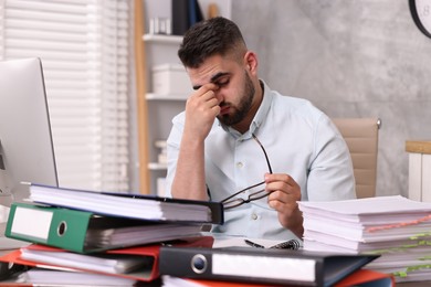 Photo of Overwhelmed man surrounded by documents at workplace in office