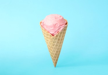 Photo of Delicious pink ice cream in waffle cone on light blue background