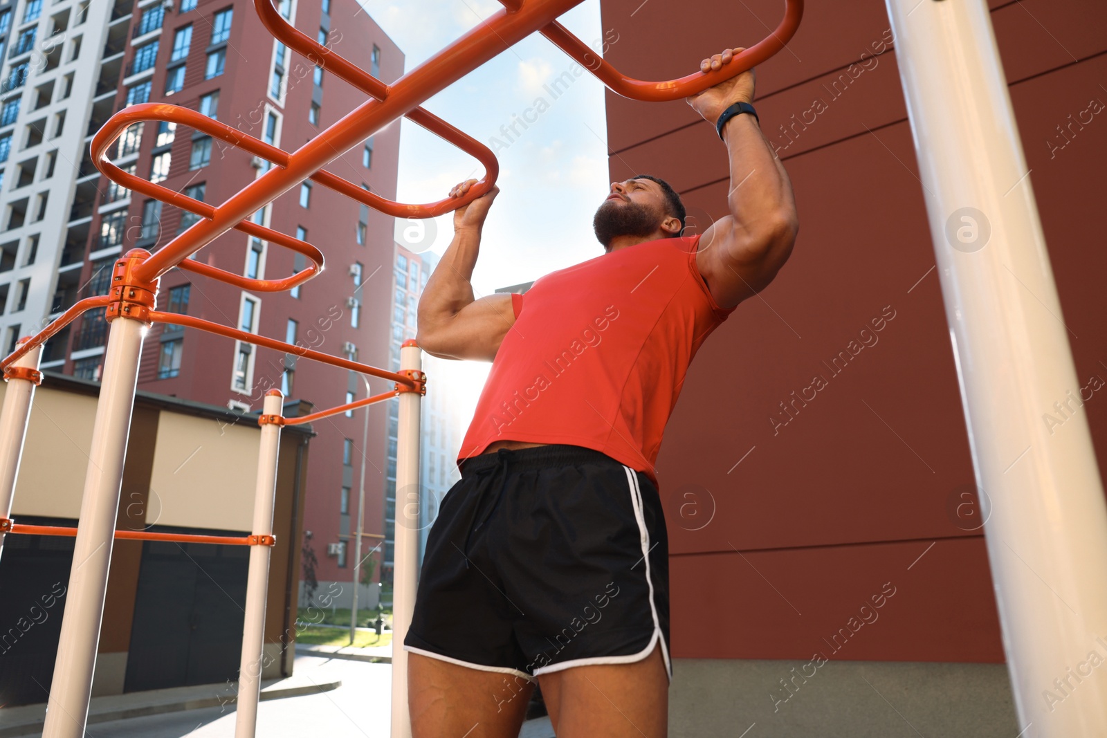 Photo of Man training on horizontal bars at outdoor gym on sunny day, low angle view