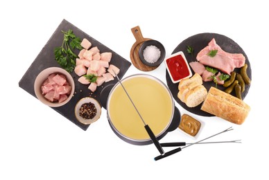 Photo of Oil in fondue pot, forks, sauces, pieces of raw meat and other products isolated on white, top view